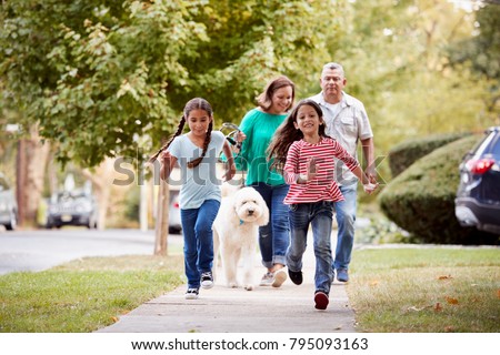 Grandparents And Granddaughters Walking Dog Along Street