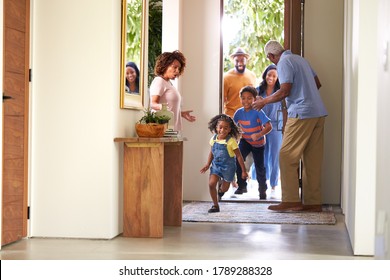 Grandparents At Home Opening Door To Visiting Family With Children Running Ahead