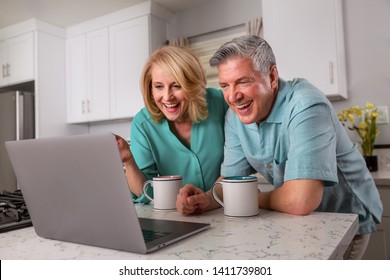 Grandparents On Computer Communicating With Grandkids Via Video Chat From Home Kitchen