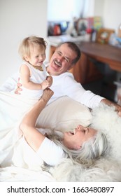 Grandparents Playing With Baby Girl On Bed