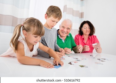 Grandparents Playing Together With Kids Holding Jigsaw Puzzle Pieces At Home