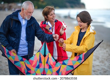 Grandparents with preteen girl preparing kite for flying on sandy beach.