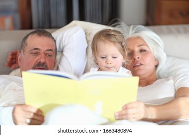 Grandparents reading with baby girl on bed - Powered by Shutterstock