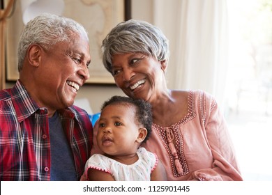 Grandparents Sitting On Sofa With Baby Granddaughter At Home