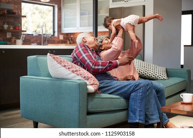 Grandparents Sitting On Sofa Playing With Baby Granddaughter At Home - Powered by Shutterstock