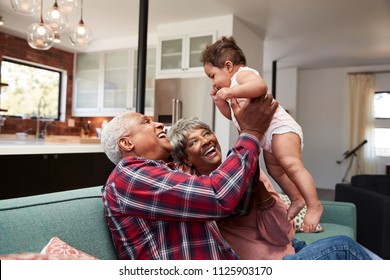 Grandparents Sitting On Sofa Playing With Baby Granddaughter At Home