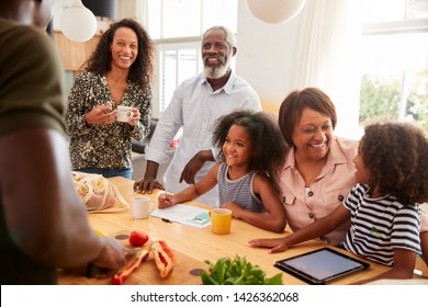 Grandparents Sitting At Table With Grandchildren Playing Games As Family Prepares Meal