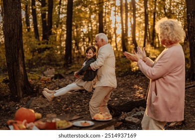 Grandparents spending time on a picnic with their granddaughter while grandfather is carrying and being goofy with little girl - Powered by Shutterstock