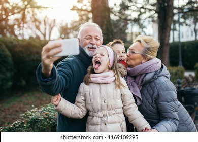 Grandparents taking selfie photo with their grandchildren in city park. 