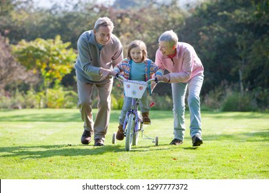 Grandparents Teaching Granddaughter To Ride Bike With Training Wheels