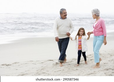 Grandparents Walking Along Beach With Granddaughter