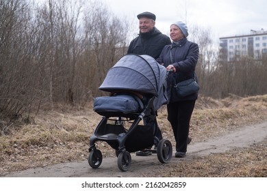 Grandparents Walking With A Stroller In Park On Early Spring.