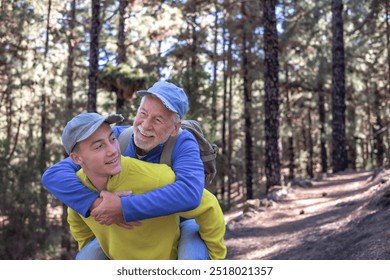 Grandson carries his grandfather on shoulders during excursion day in forest. Smiling multi-generational family couple enjoying healthy lifestyle and nature together - Powered by Shutterstock