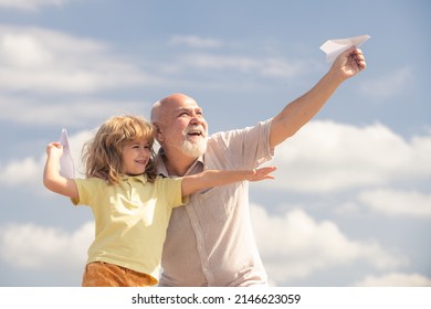 Grandson Child And Grandfather With Toy Paper Plane Against Summer Sky Background. Child Boy With Dreams Of Flying.