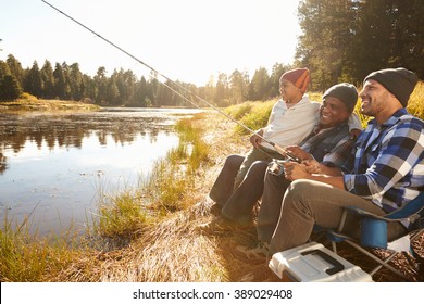 Grandson With Father And Grandfather Fishing By Lake