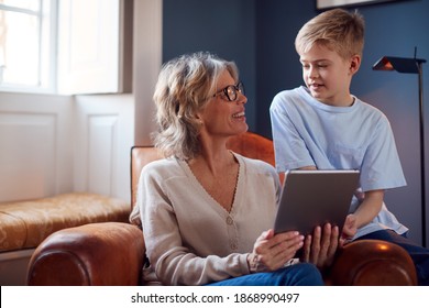 Grandson With Grandmother Sitting In Chair Playing On Digital Tablet At Home Together - Powered by Shutterstock