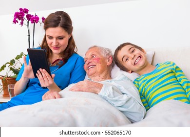 Grandson visiting grandmother in the nursing home, a young nurse spending time with them, holding a digital tablet. - Powered by Shutterstock