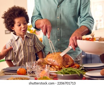 Grandson Watching Grandfather Carve Turkey As Family Celebrate Thanksgiving With Meal At Home