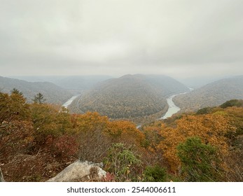 At Grandview Overlook in New River Gorge National Park, a foggy autumn day reveals the river winding through vibrant hills. Fall foliage colors blanket the landscape, fading into the misty horizon. - Powered by Shutterstock