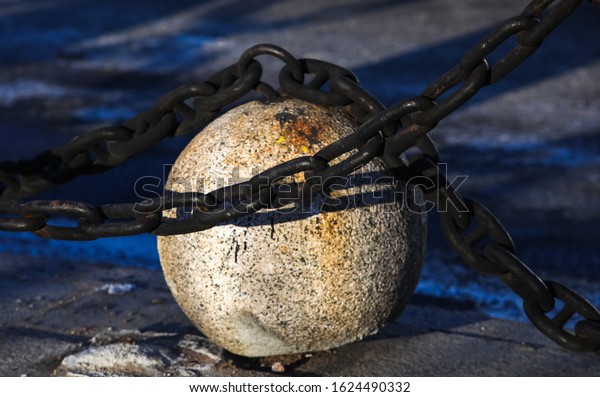 Granite ball and metal chain close-up on the\
pavement in summer