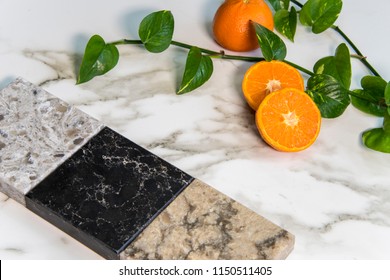 Granite, Marble And Quartz Square Color Samples Of Kitchen Countertop Over White Carrara Marble Natural Stone Slab And Fresh Oranges On It