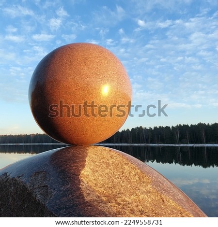 Granite sculpture. A huge round stone miraculously keeps balance. Modern Art. A fragile balance.