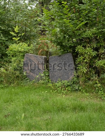 Granite stone sculpture standing split into two parts in a lush green garden setting
