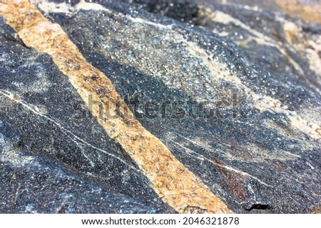 Granite stone texture up close. Intrusive rocks background. Large untreated gray-blue stone surface with a yellow, golden, beige stripe. Natural material. Marble rocky macro photography backdrop.