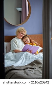 Granny And Child Girl Read A Book Before Bed. Evening Ritual Before Bedtime, Communication Between Generations, Retired Female Is Spending Time With Grandchildren, Relaxing And Teaching