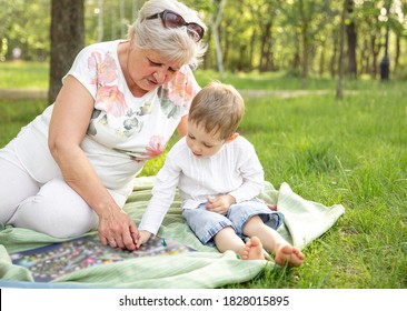 Granny And Child Sitting On The Floor And Playing Classic Table Games. Happy Grandmother And Grandson Playing Board Game Together In The Summer Park. Happiness, Family Vacation, Fun Leisure Concept