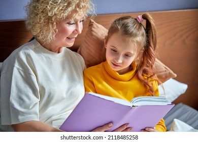 Granny And Daughter Read A Book Before Bed. Evening Ritual Before Bedtime, Communication Between Generations, Retired Female Is Spending Time With Grandchildren, Relaxing And Teaching