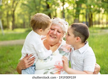 Granny with grandsons enjoying time together in summer park. Happy grandmother with grandchildren. Portrait of smiling family relaxing. Senior woman hugging boys in nature.Bonding of relatives