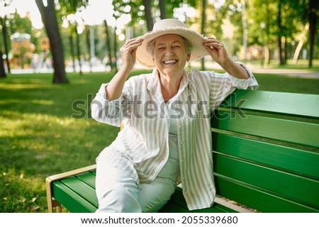 Granny in hat sitting on the bench in summer park