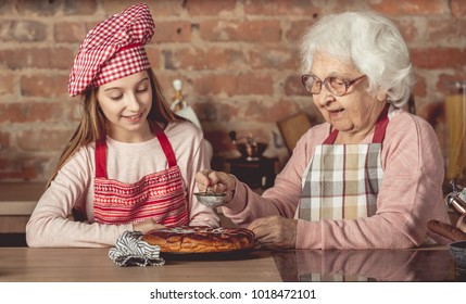 Granny with her little chef girl sprinkle with powder hot homemade pie