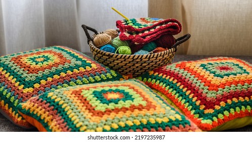 Granny square crochet. Home made creations. Colorful wool yarns in a straw basket on a couch. Handmade knitting, knit pillows, and a cute atmosphere. - Shutterstock ID 2197235987