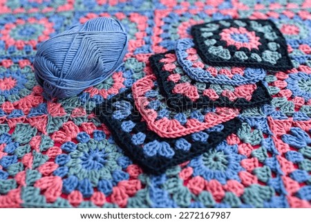 Granny square crochet motifs contrast colors and a skein of yarn placed on an afghan. Texture of crochet patterns.