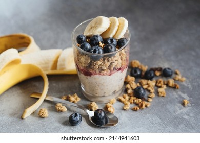 granola with banana and blueberries with yogurt in glass cup on gray background, healthy diet breakfast muesli with yogurt and fruits - Shutterstock ID 2144941603
