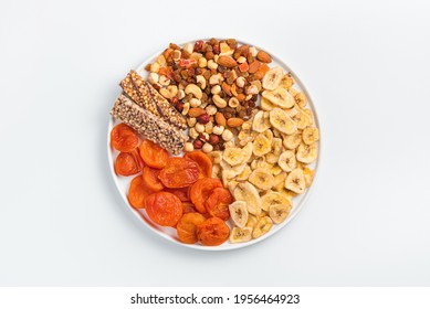 Granola Bar, Dried Apricots, Dried Bananas, Nuts And Dried Fruits In A White Flat Plate On A Light Background. Top View, Horizontal. Healthy Food.