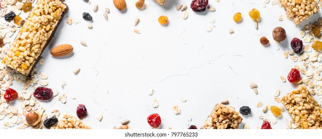 Granola bar and ingredients on a white stone table. Cereal granola bar with nuts, fruit and berries. Top view long banner format.