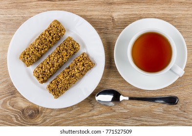 Granola Bar In White Plate, Cup Of Tea On Saucer, Teaspoon On Wooden Table. Top View