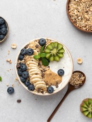Granola Bowl. Yogurt And Muesli With Fresh Fruits (banana Slices, Kiwi, Blueberry) And Peanut Butter In Ceramic Bowl. Top View. Close Up Food. Gray Background. Healthy Vegetarian Breakfast Or Lunch. 