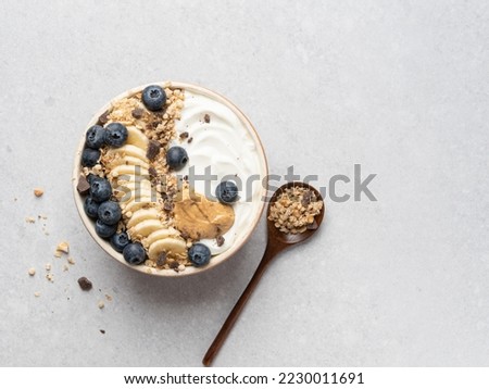 Granola bowl. Yogurt and muesli with fresh banana slices, blueberry and peanut butter in ceramic bowl. Top view. Copy space. Gray background. Healthy vegetarian breakfast or lunch. Morning tasty meal.