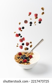 Granola flakes flying in the air with hazelnuts, raspberries, blueberries. Healthy homemade breakfast with yogurt in white bowl on light background. Isolate with copy space - Shutterstock ID 2217473725