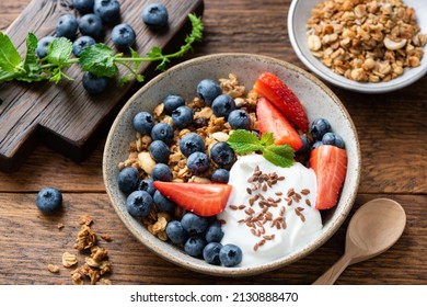 Granola with greek yogurt and berries strawberry blueberry in bowl topped with flax seeds. Rustic wooden table background. Clean eating, dieting concept - Powered by Shutterstock