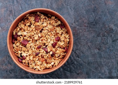 Granola with nuts and dried fruit on a dark background. Homemade granola in a clay bowl. Top view. Copy space