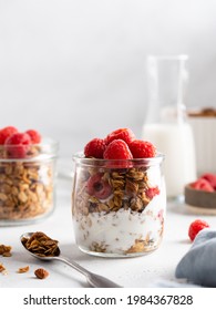 Granola (oatmeal muesli) with yoghurt in glass served with fresh raspberry, honey and milk. Tasty vegetarian breakfast, snack or dessert. Healthy eating concept. Copy space. Morning table background.