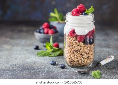 Granola Parfait with Yogurt, oat granola, fresh berries, honey and mint leaves in tall glass jar, copy space - Powered by Shutterstock