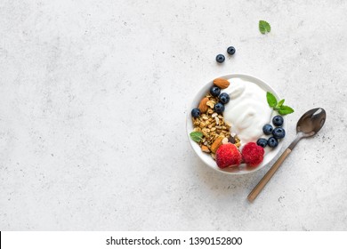 Granola with yogurt and berries for healthy breakfast. Bowl of greek yogurt with granola, almonds, blueberries and strawberries, top view, copy space.