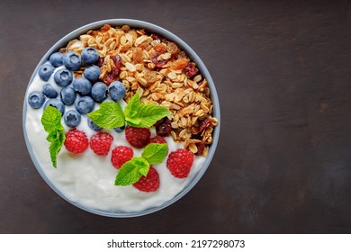 Granola with yogurt and berries on a dark brown background. Healthy breakfast with yogurt, baked granola, blueberries and raspberries. Top view. Copy space - Powered by Shutterstock