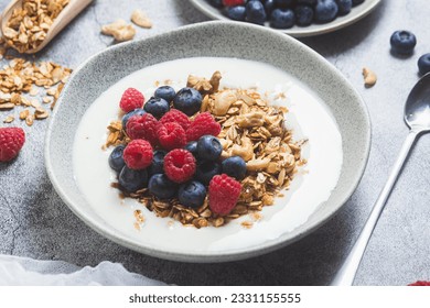 Granola with yogurt, raspberries, blueberries in a plate on a gray background